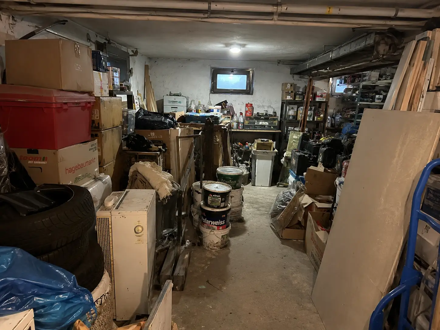 Vollgestellte Garage mit Kartons, Reifen, Farbeimern und Werkzeug an den Wänden