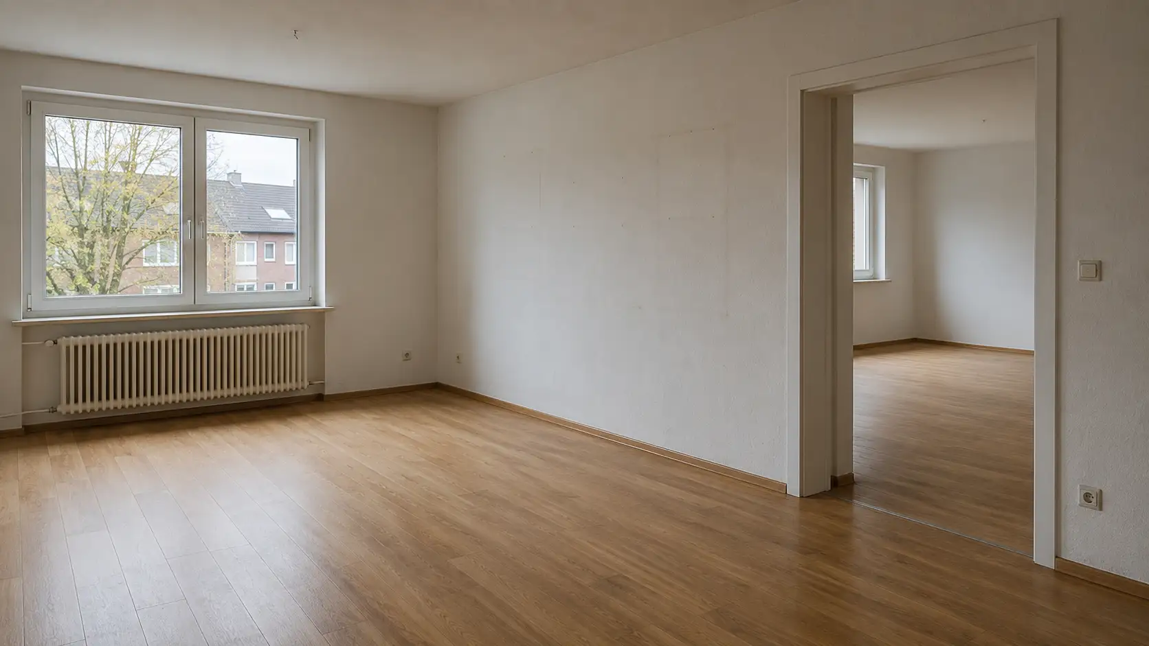 Leer geräumte helle Wohnung mit Parkettboden, Heizkörper am Fenster und Durchblick in den nächsten Raum