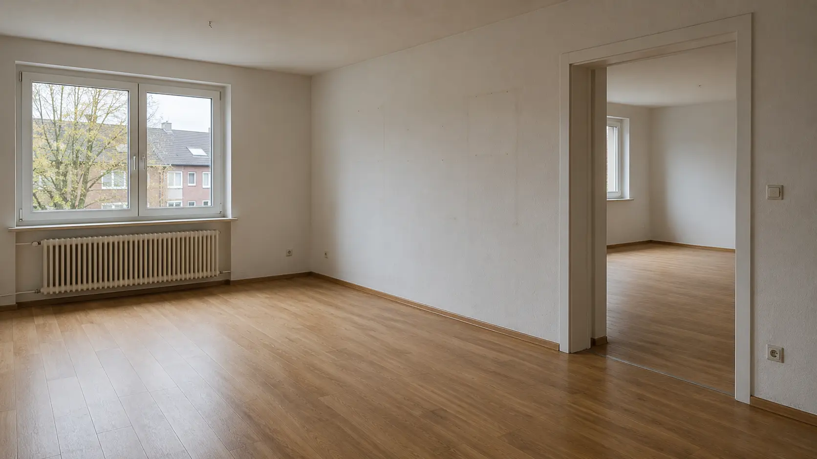Leer geräumte helle Wohnung mit Parkettboden, Heizkörper am Fenster und Durchblick in den nächsten Raum