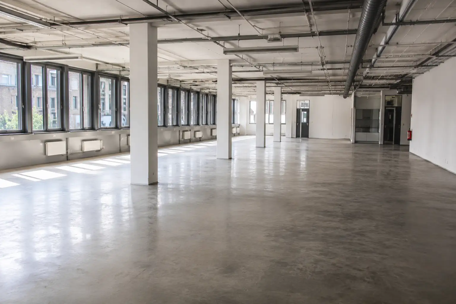 Leer geräumte Gewerbefläche mit Betonboden, Stützen und langer Fensterfront