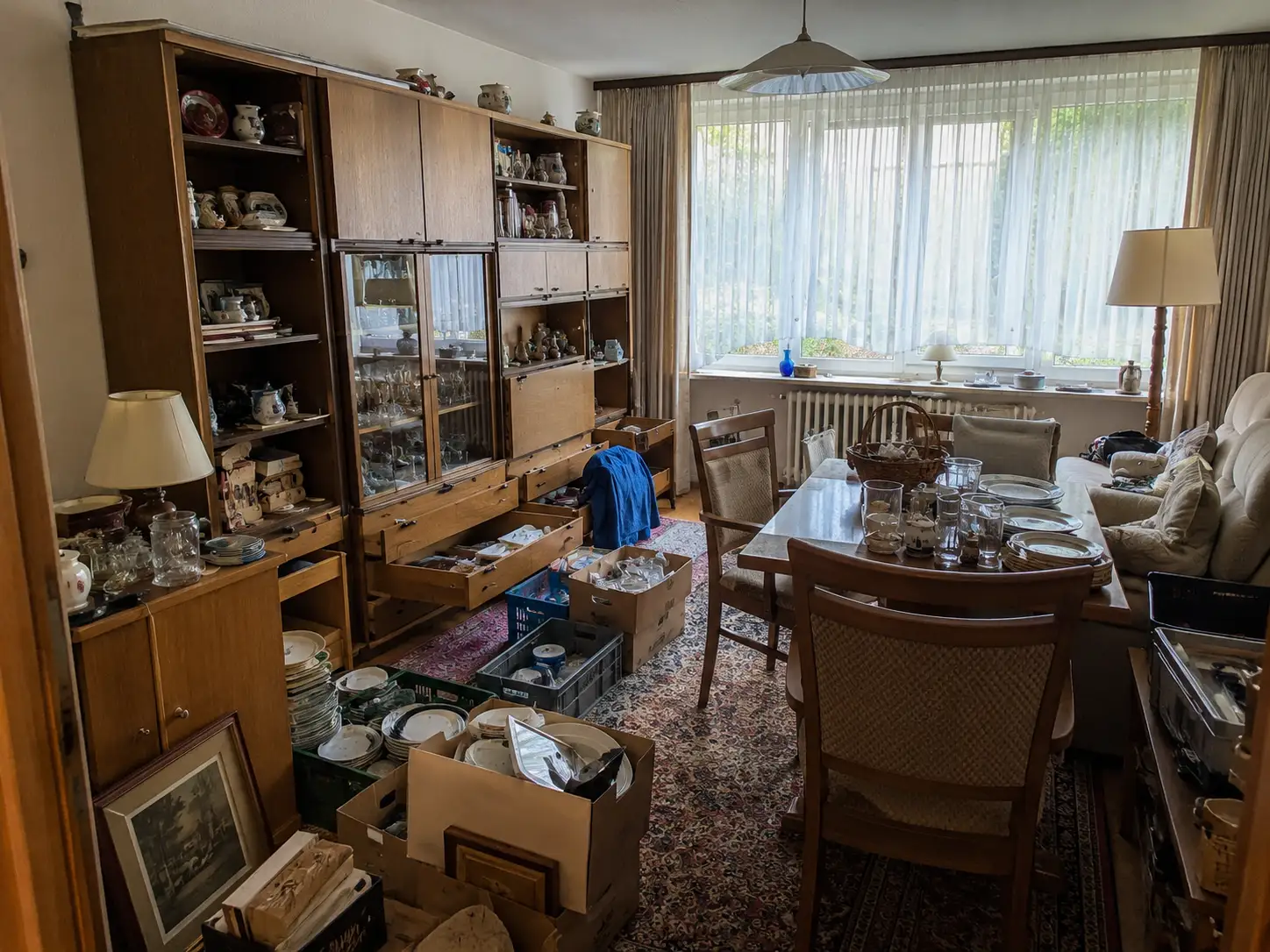Wohnzimmer mit gefüllter Vitrine, Porzellan und gestapelten Kisten während der Haushaltsauflösung