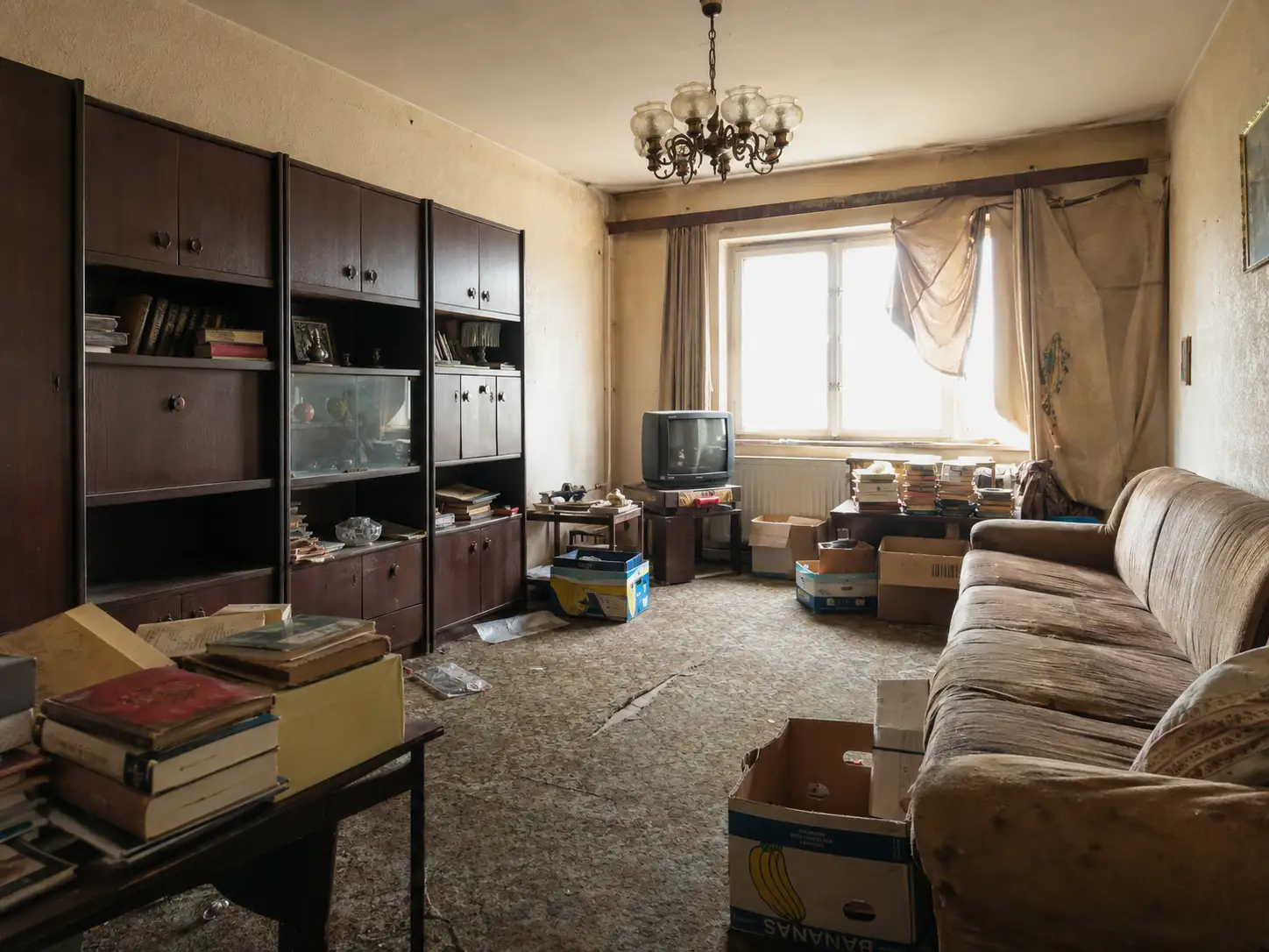 Vollgestelltes Wohnzimmer mit Schrankwand, altem Sofa und gestapelten Kartons